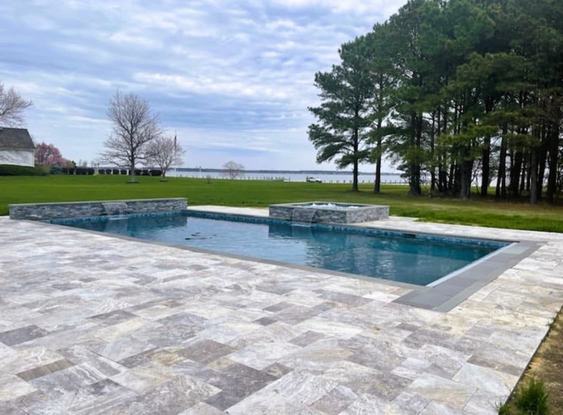 Premium travertine pool decking with raised spa on a waterfront property.