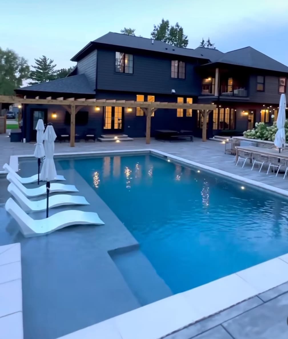 Modern pool with premium stone decking and pergola at dusk.